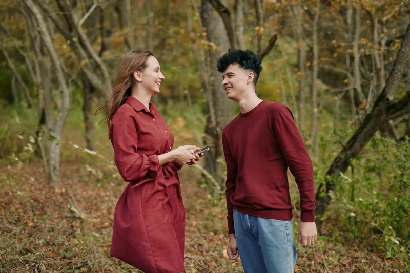 A candid outdoor portrait of two young people sharing a laugh in autumn woods, natural body language and warm tones conveying authenticity and credible connection between friends and companions.