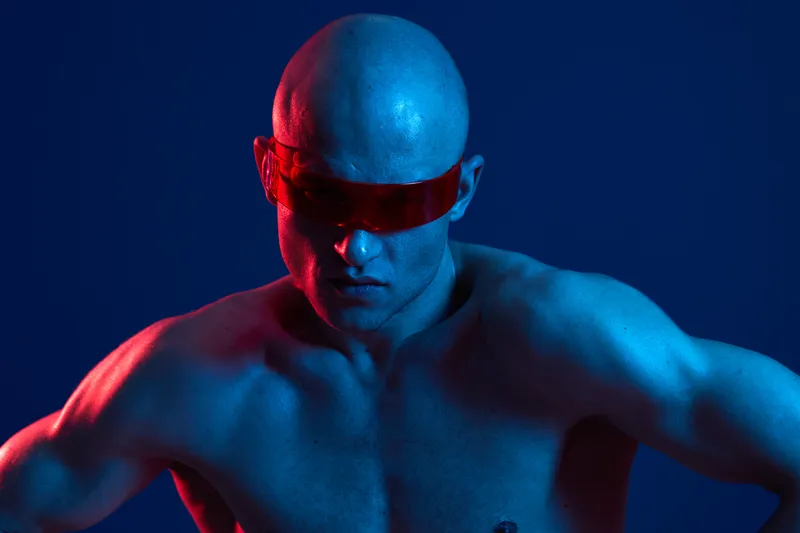 Muscular man with sunglasses in a dramatic blue and red light, showcasing strength and intensity. The image captures a bold, striking atmosphere.
