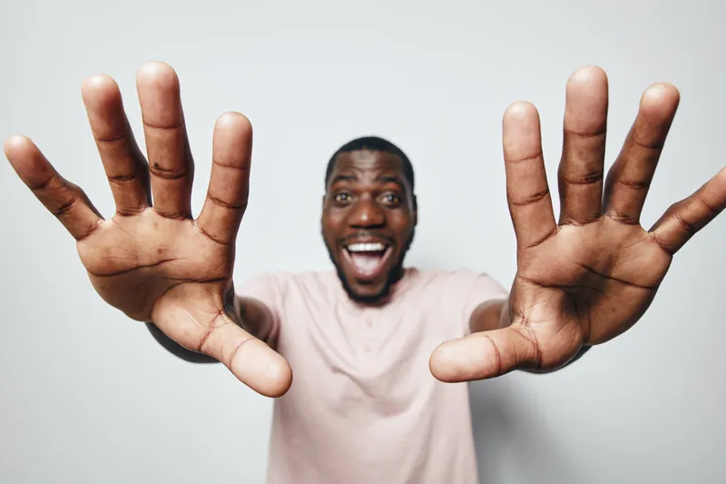 African man with dark skin smiling and reaching hands forward in excitement isolated on white background. Happy male portrait with open palms and joyful expression.