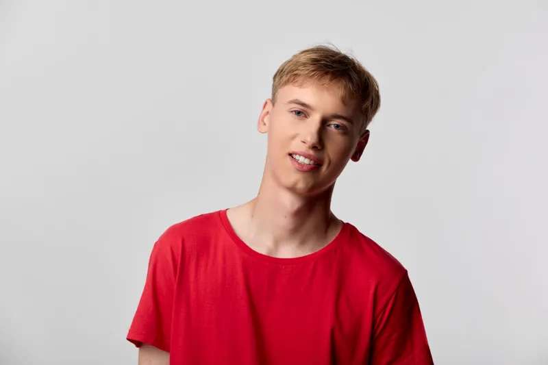Young man wearing a red t shirt in a studio setting with a relaxed expression, showcasing casual fashion and contemporary style for lifestyle and stock photography.