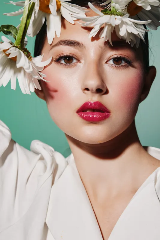 Close-up portrait of a young woman with pink glossy lips and natural makeup adorned with white flowers. Creative beauty photo with fresh and soft color palette for fashion.