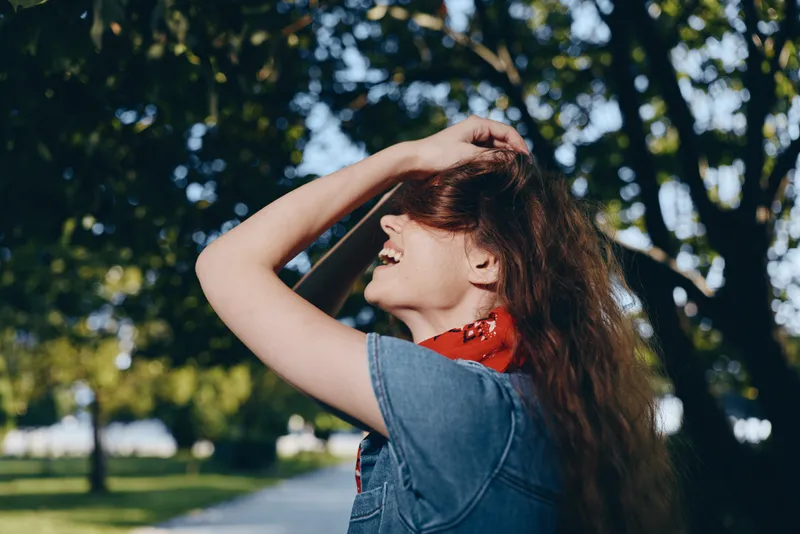 lifestyle woman with modern boho-western denim street style laughing outdoors in sunny park with film color effect and natural greenery background
