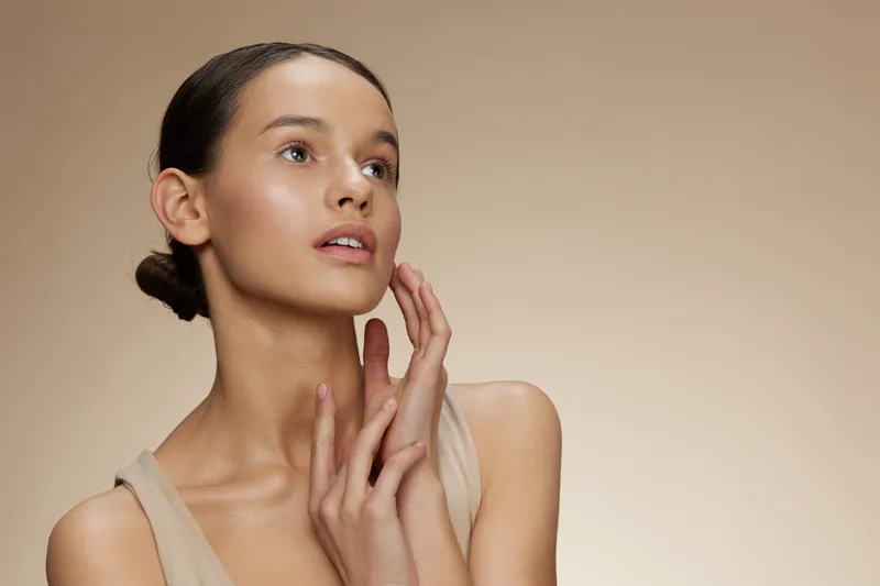 Elegant young woman in neutral toned top expressing confidence against a soft beige background Perfect for beauty and skincare concepts