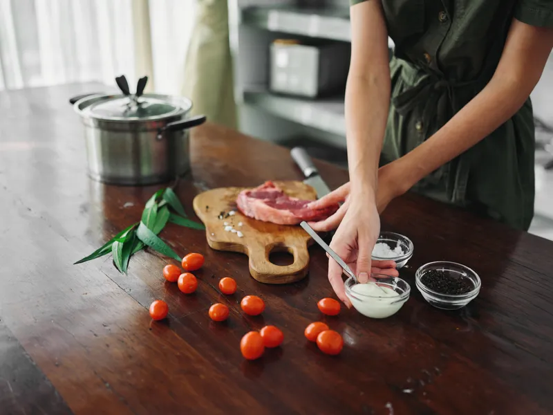 Женщина на кухне готовит ужин из мяса, овощей и специй на деревянном столе на фоне стильной кухни, крупный план рук, образ жизни