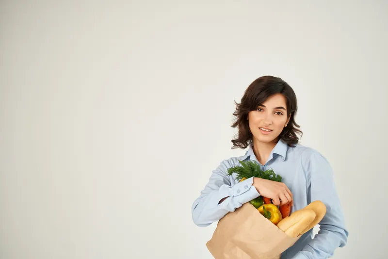 Симпатичная брюнетка в голубой рубашке с продуктовой сумкой, органической едой