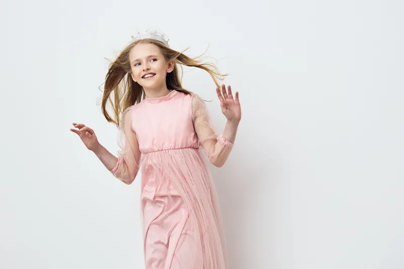 Young girl in a pink dress joyfully dancing against a minimalistic light background, capturing the essence of childhood happiness and innocence