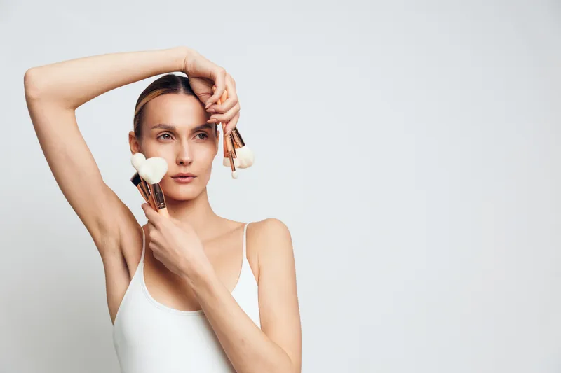 Woman applying white cream to face, skincare routine for beauty and wellness, self care in studio portrait. Soft studio light and brush application create calm confidence with hair grooming.