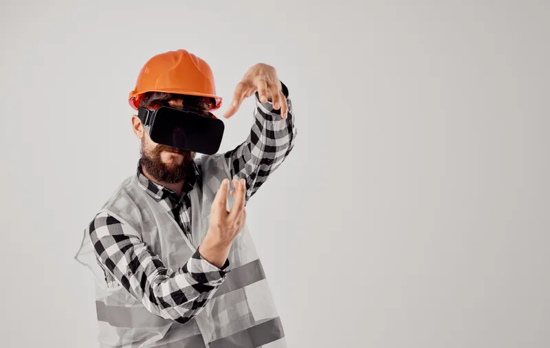 Строитель в оранжевой каске и 3D-очках жестикулирует руками