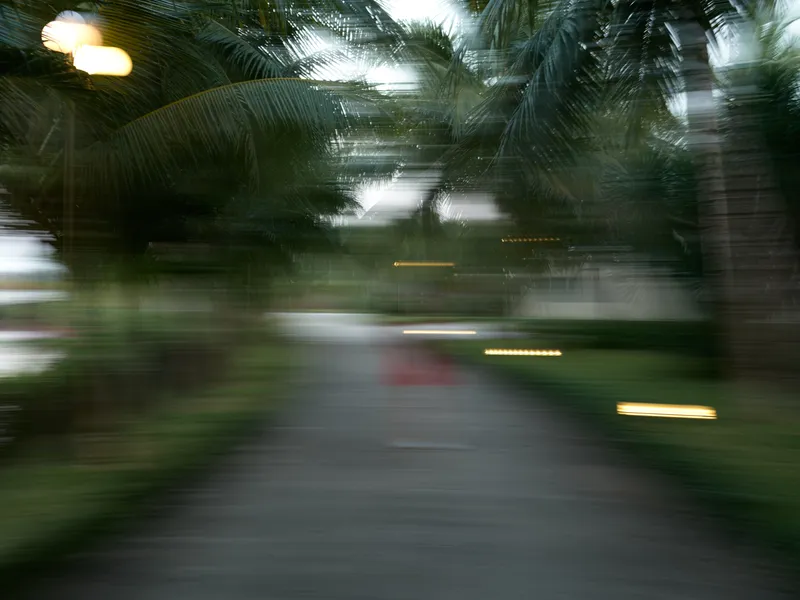 Abstract motion blur of a tropical pathway surrounded by lush green palm trees, creating a dynamic and vibrant jungle atmosphere with natural light and a mysterious mood.