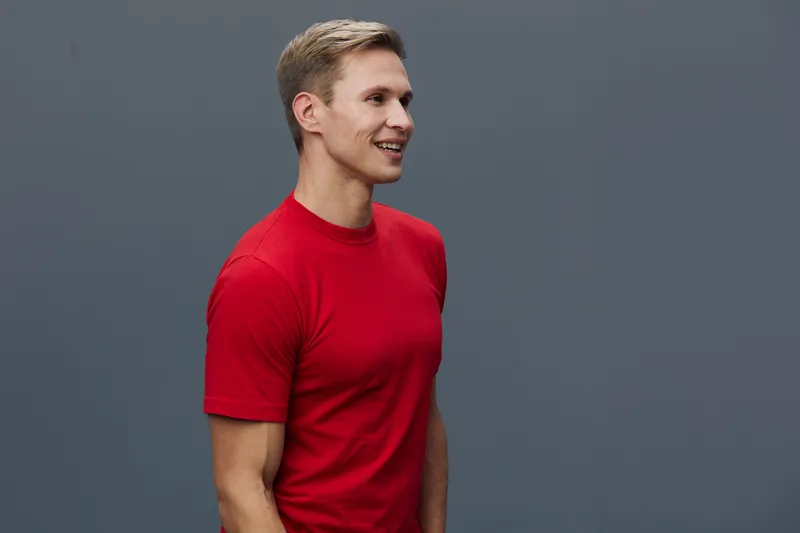 Young smiling caucasian man wearing red t-shirt standing side view looking forward isolated on gray background casual style digital detox concept healthy lifestyle