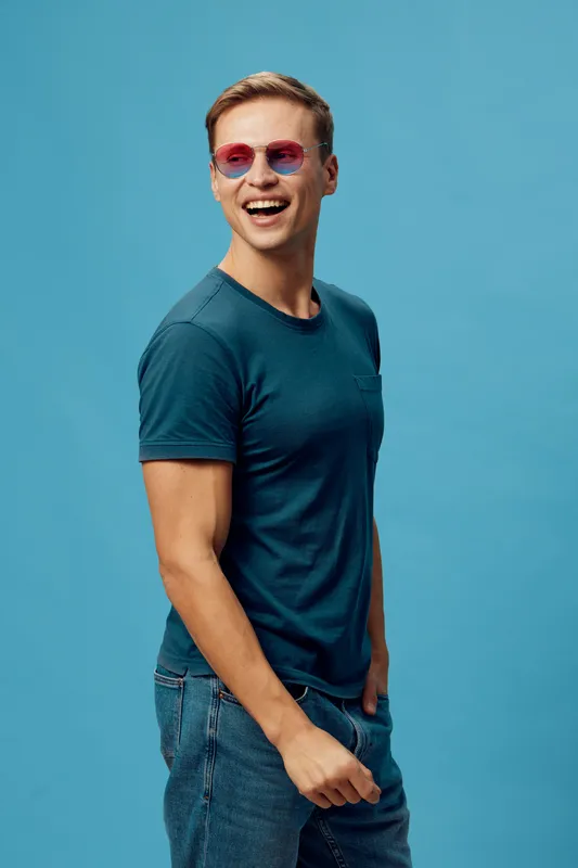 smiling young man wearing pink sunglasses casual blue t-shirt jeans isolated on blue background digital nomad work lifestyle technology concept