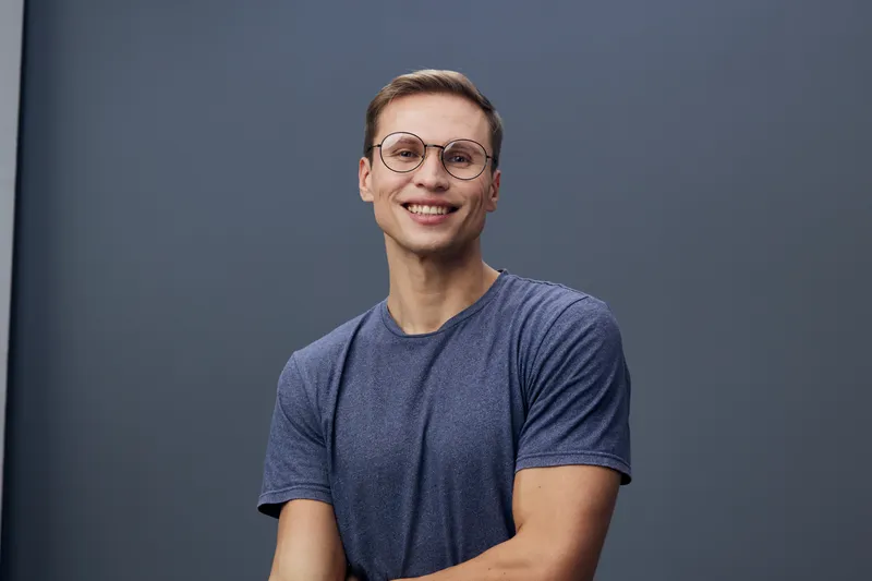 smiling young caucasian man wear glasses blue t-shirt look camera sit pose isolated on gray background digital detox mental health concept