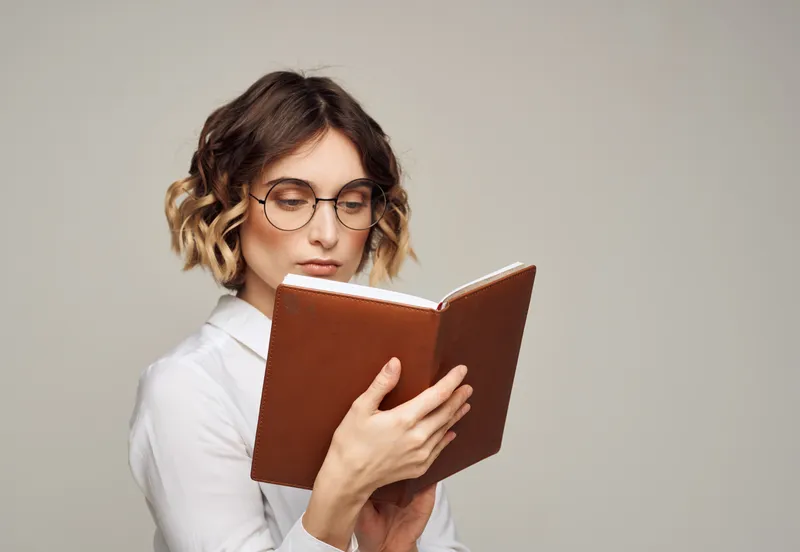 Женщина в очках держит в руке книгу на сером фоне