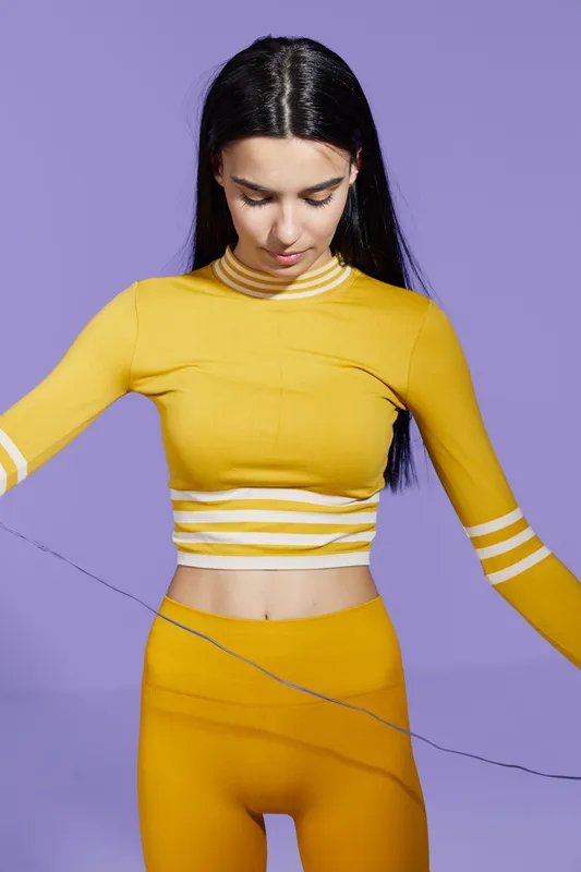 woman sport fitness performing stretching exercise in bright yellow workout outfit with purple background, focusing on body movement and flexibility indoors