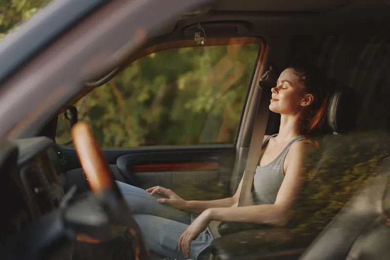 Young woman enjoying a moment of peace in a car, with sunlight illuminating her face, reflecting a sense of calm and tranquility during a road trip