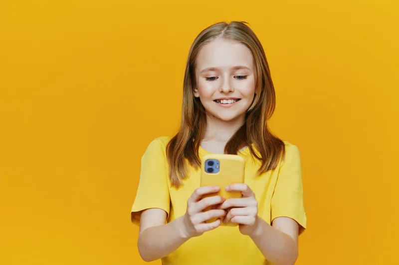 Happy young girl using smartphone against bright yellow background, wearing casual yellow outfit, embodying joy and connectivity in modern lifestyle