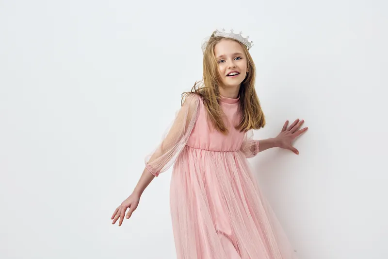 Cheerful girl in a pink tulle dress, joyfully posing against a light background, embodying elegance and innocence in a fashion forward style