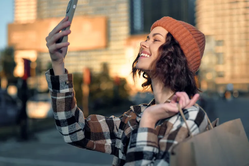 woman selfie shopping city smile beanie sunset portrait of a young female with paper bag, candid authenticity and golden hour glow capturing joyful mindful living and emotional storytelling