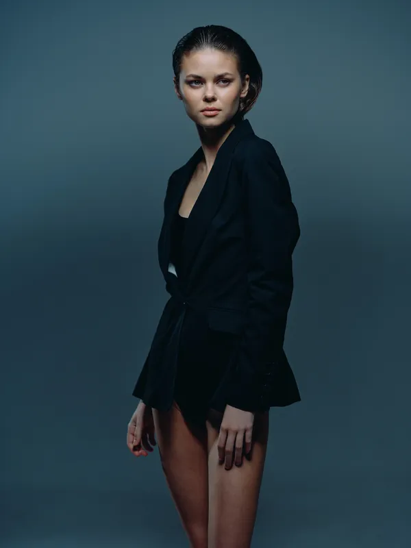 Serious woman in black blazer standing against dark background, confident pose, studio portrait, professional fashion style