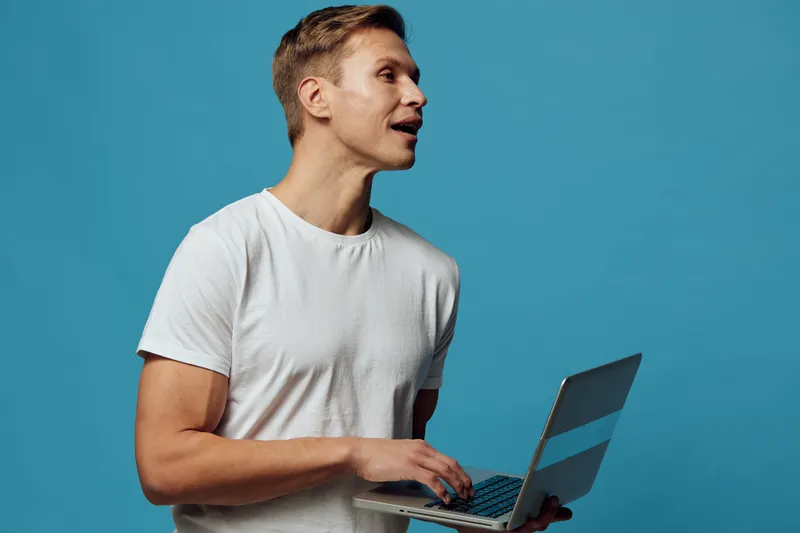 young caucasian man working with laptop speak in video call wear white t-shirt isolated blue background remote digital nomad concept