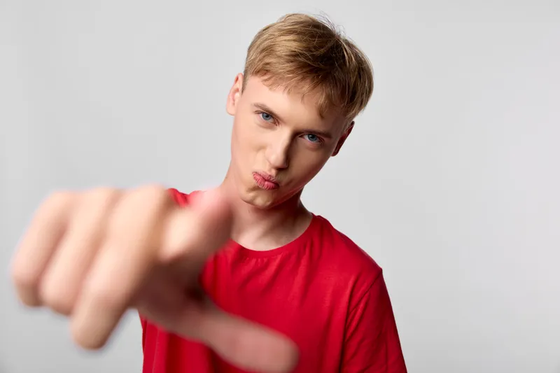 Man in a red t shirt points at the camera with a playful, confident expression in a studio setting, capturing direct communication, bold gesture, and energetic lifestyle vibe against a clean backdrop
