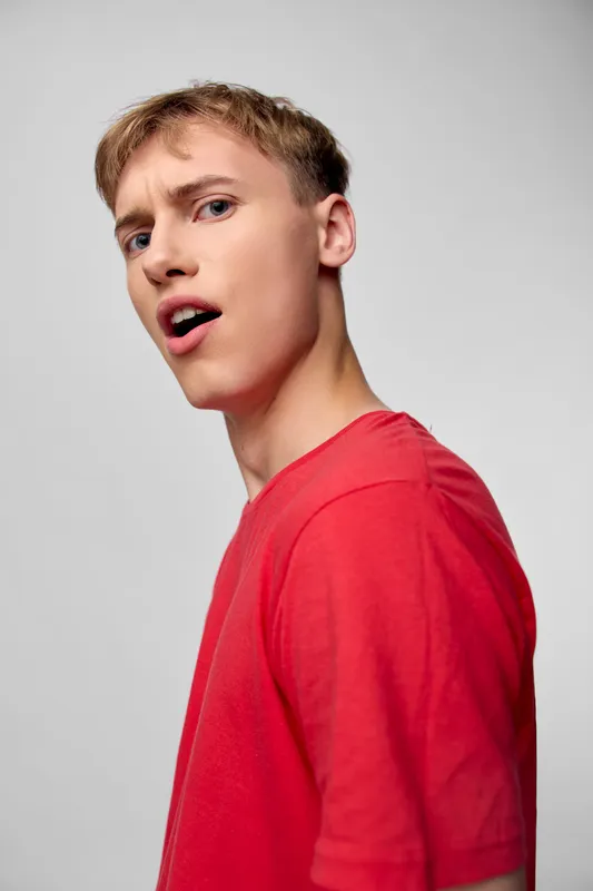 Young man in a red shirt with a surprised expression, studio shot, bright lighting, casual fashion, expressive pose, energetic mood and youthfulness captured against a clean neutral background