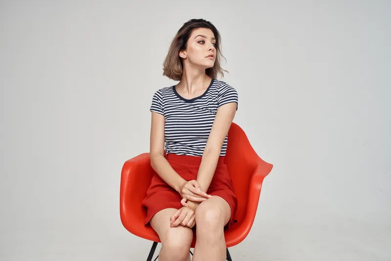 Красивая женщина в модной одежде сидит на красном стуле на светлом фоне