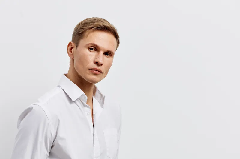 Confident young Caucasian man wearing white shirt looking at camera with neutral expression isolated on plain white background studio portrait. People lifestyle concept