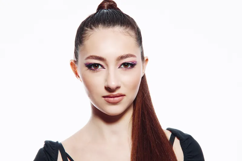 Portrait of a young woman with sleek long ponytail and creative pastel pink makeup. Close-up on white background, highlighting beauty, fashion, and artistic style concepts.