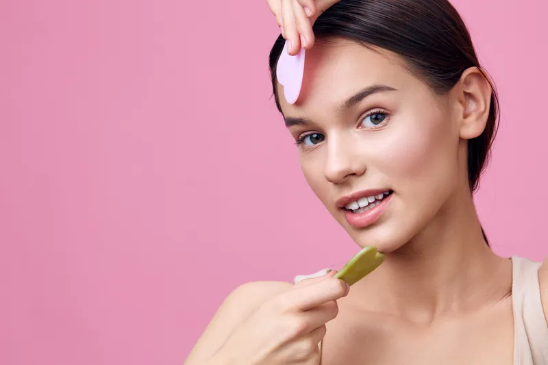 Young woman using a skincare tool for facial treatment against a soft pink background, expressing joy and freshness Skincare, beauty, wellness, self care, pink, tools, facial