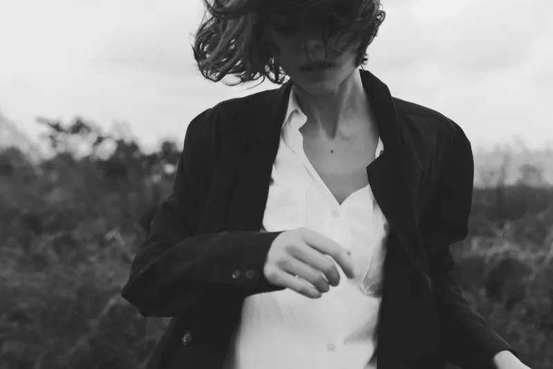 Woman in a jacket and white shirt outdoors, captured in black and white with a moody candid vibe, highlighting street style, movement and texture in a dramatic monochrome frame