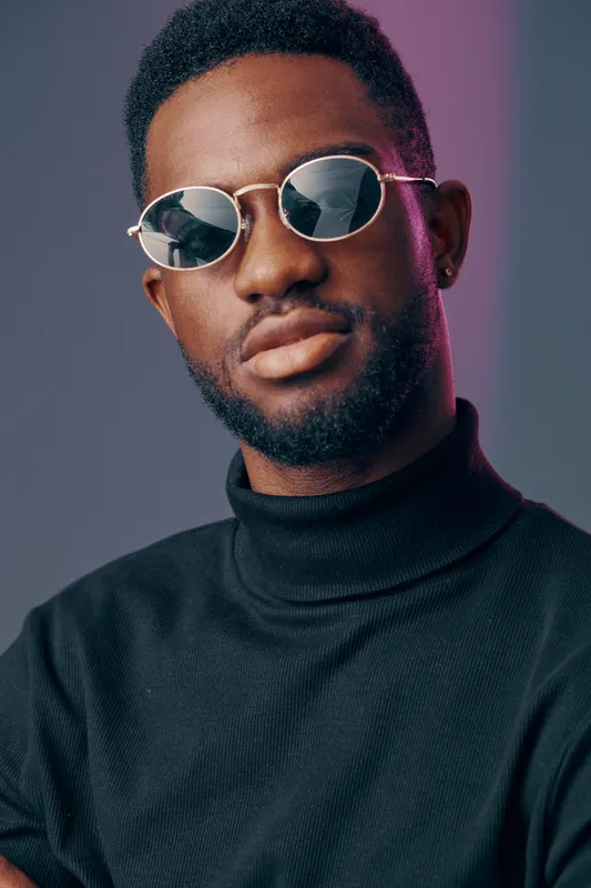 Stylish young Black man wearing sunglasses and a turtleneck sweater, showcasing confidence and modern fashion against a colorful background