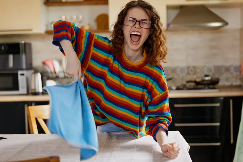 Smiling woman in a colorful striped sweater ironing clothes at home kitchen, a cheerful lifestyle moment highlighting domestic chores and self care with warm lighting.