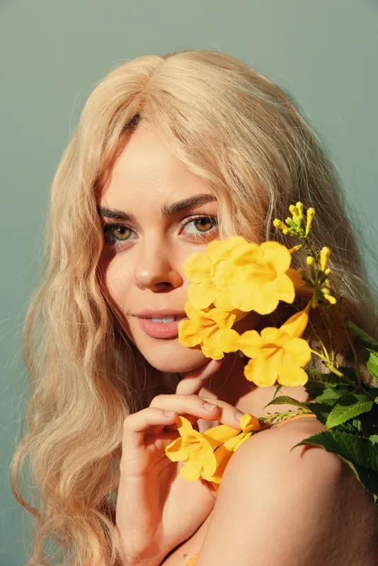Потрясающая молодая женщина с blond-волосами нежно держит желтые цветы, излучая безмятежность и красоту