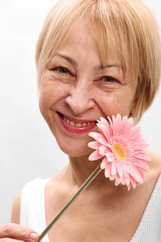 Woman, senior, smile, pink, flower, blossom, happiness, spring, beauty, portrait, blond hair and gentle eyes, pink bloom close to her lips, soft wrinkles, closeup face, white background, calm joy