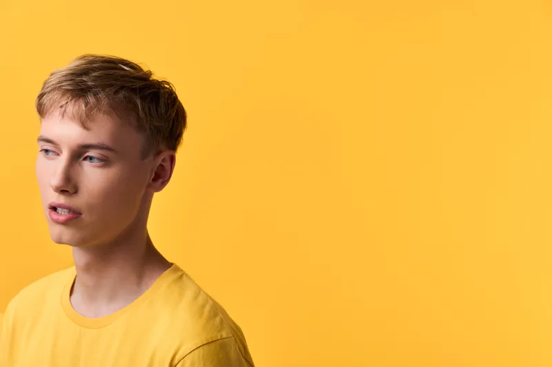 Man in yellow shirt against a monochrome yellow backdrop, thoughtful pose, clean studio composition, warm color mood, contemporary fashion vibe.