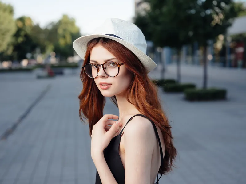 Привлекательная женщина идет по улице в шляпе и очках