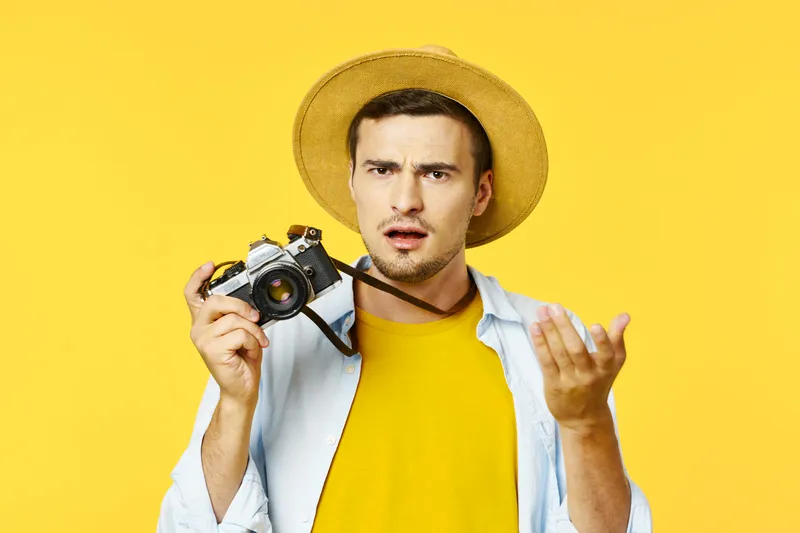Удивленный мужчина на желтом фоне держит в руке фотоаппарат