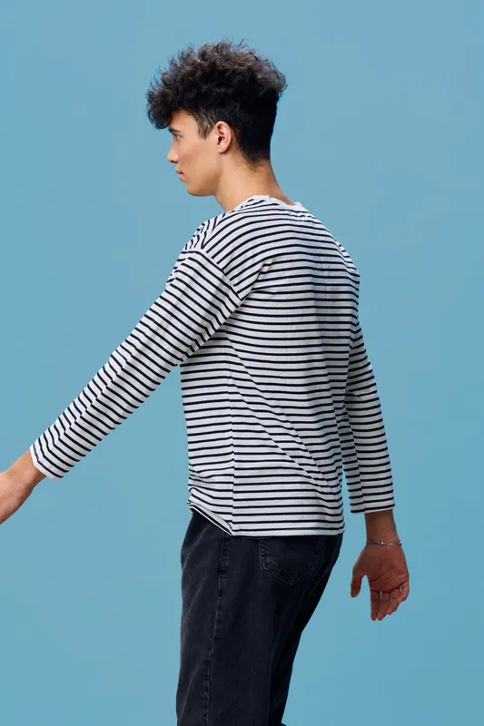young man in striped shirt with curly hair walking against blue background, casual style and relaxed posture showing modern fashion and youth trends