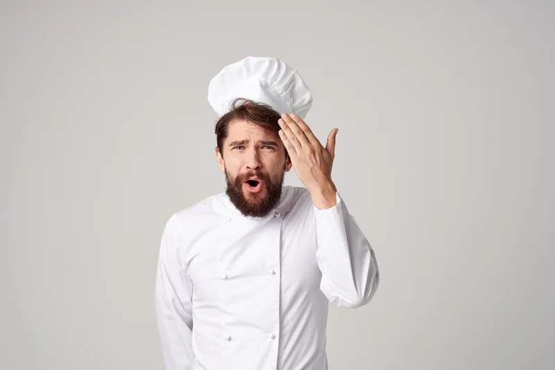 Повар-мужчина в форме шеф-повара готовит, демонстрируя эмоции гурмана на светлом фоне