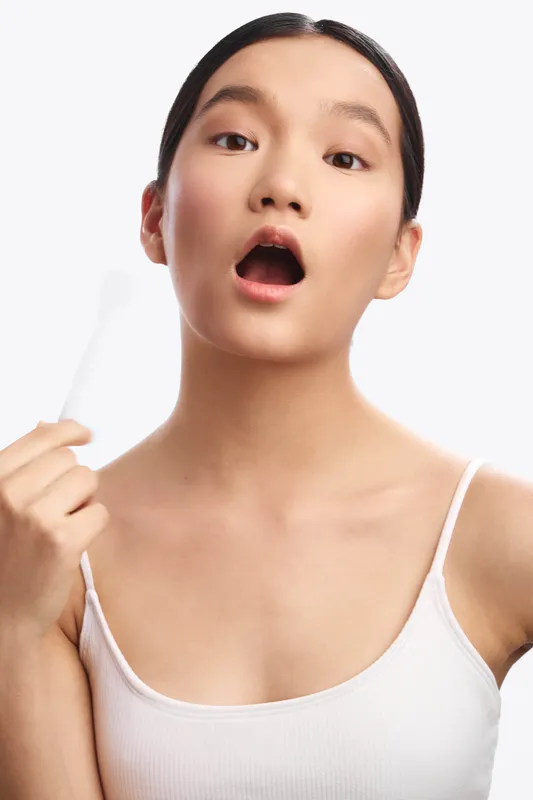 asian woman with a surprised expression stands against a clean studio background, wearing a light tank top. this expressive moment conveys curiosity and immediacy.