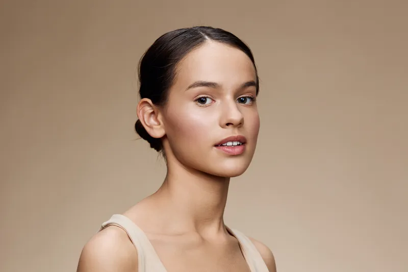 Natural portrait of a young Caucasian woman with a smooth complexion, elegant hairstyle, and soft expression against a neutral background