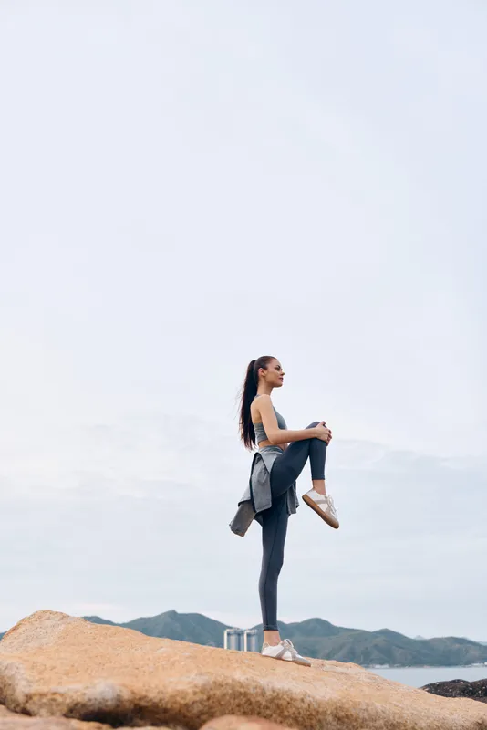 Athletic woman practicing yoga on rocky beach wearing activewear, showcasing a peaceful expression and natural surroundings in a serene outdoor setting