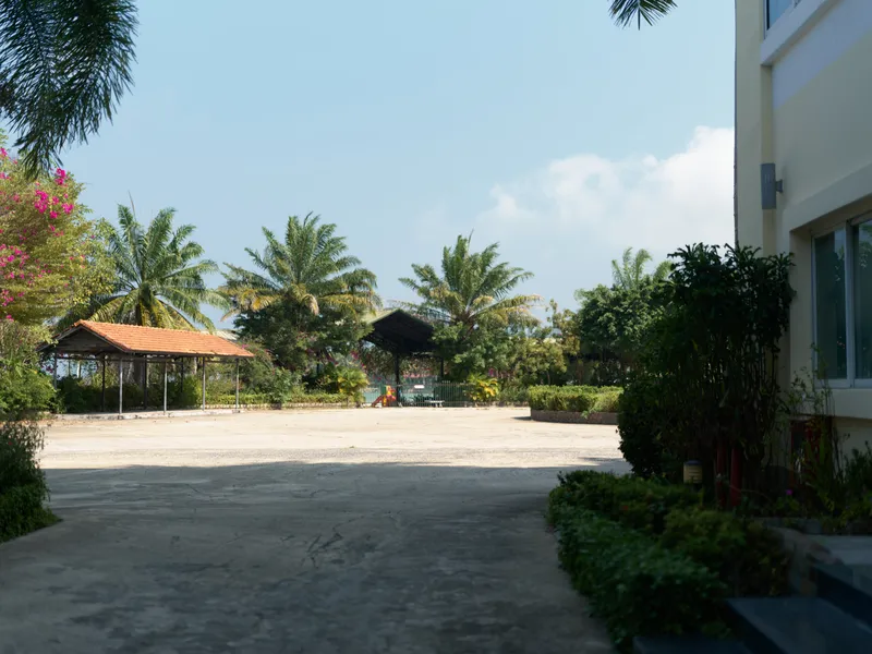 empty outdoor courtyard with tropical palm trees and small shaded pavilions under clear blue sky, bright sunny day with natural greenery around