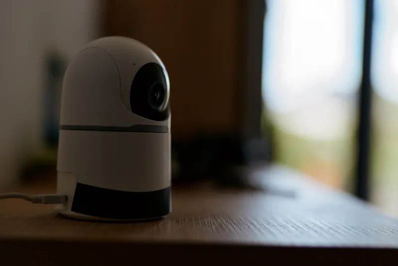 Close up of a small dome security camera on a wooden desk in a dimly lit home office, ready for monitoring, with soft background blur creating a calm modern surveillance vibe.