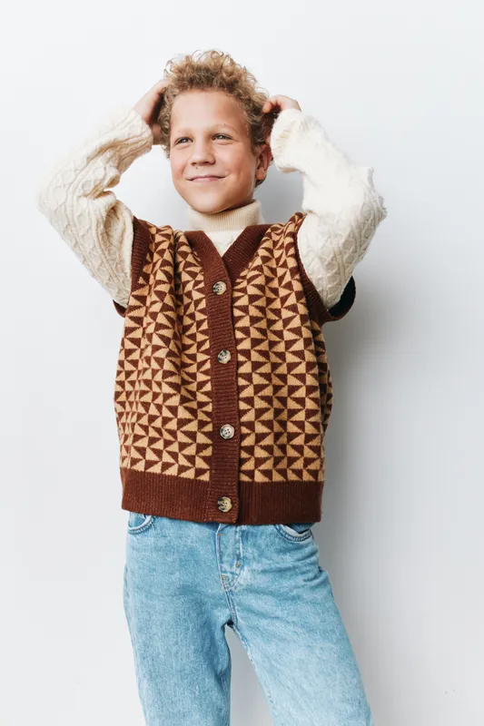 A joyful child poses confidently in a bright studio, wearing a textured knit vest and cozy sweater, highlighting authenticity and a playful school life vibe.