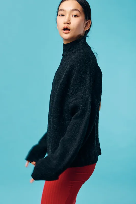 Young woman wearing black sweater and red pants posing on blue background for fashion style portrait. Casual outfit, trendy look, and confident model with natural expression in studio lighting.