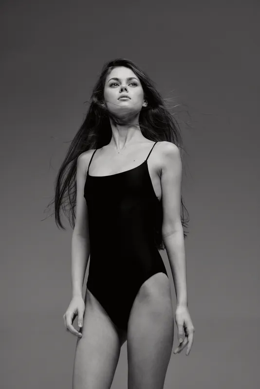 Black and white portrait of a young woman in a black swimsuit with long hair looking confident.