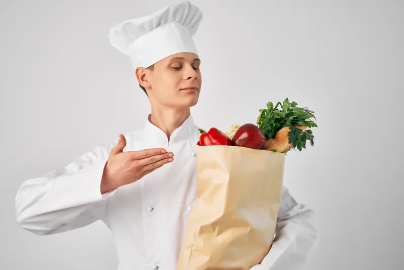 Мужчина в униформе шеф-повара с упаковкой продуктов занимается доставкой из ресторана