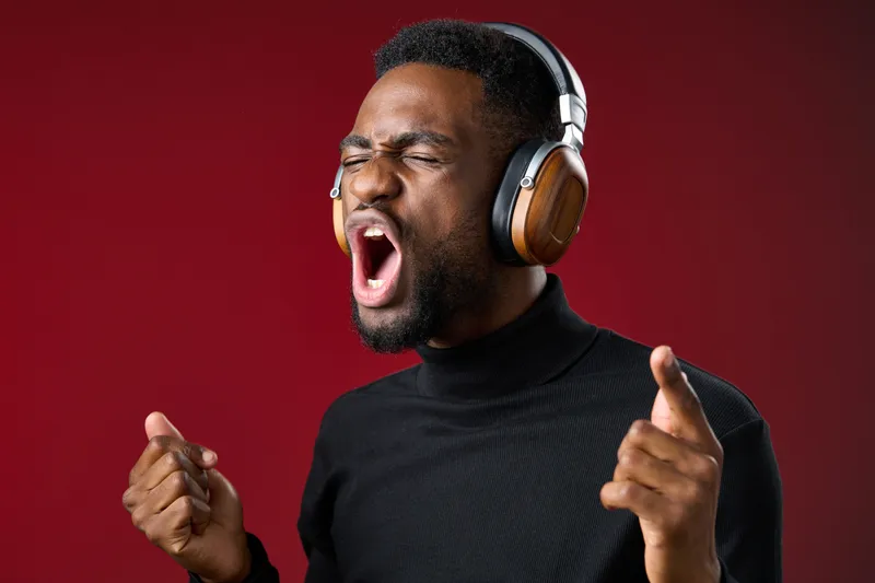 Young Black man enjoying music with headphones, expressing excitement against a vibrant red background, showcasing lively emotions and energy in a modern style